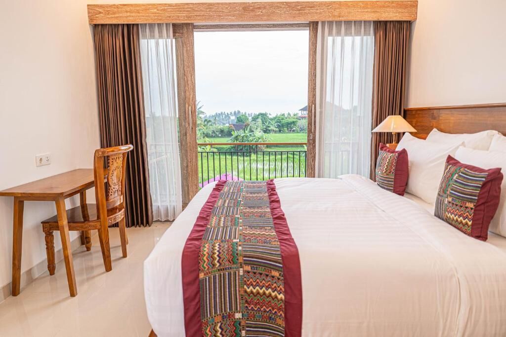 A hotel room with a bed, a desk, a chair, and a view of a green landscape through large windows.
