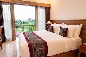 A hotel room with a large bed, a nightstand, a lamp, and a view of greenery outside. - Dauh Nyuh (Mas)