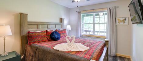 Un lit bien fait, agrémenté d’un coussin décoratif en forme de cygne, un ventilateur de plafond, une lampe de chevet et une fenêtre avec des rideaux.