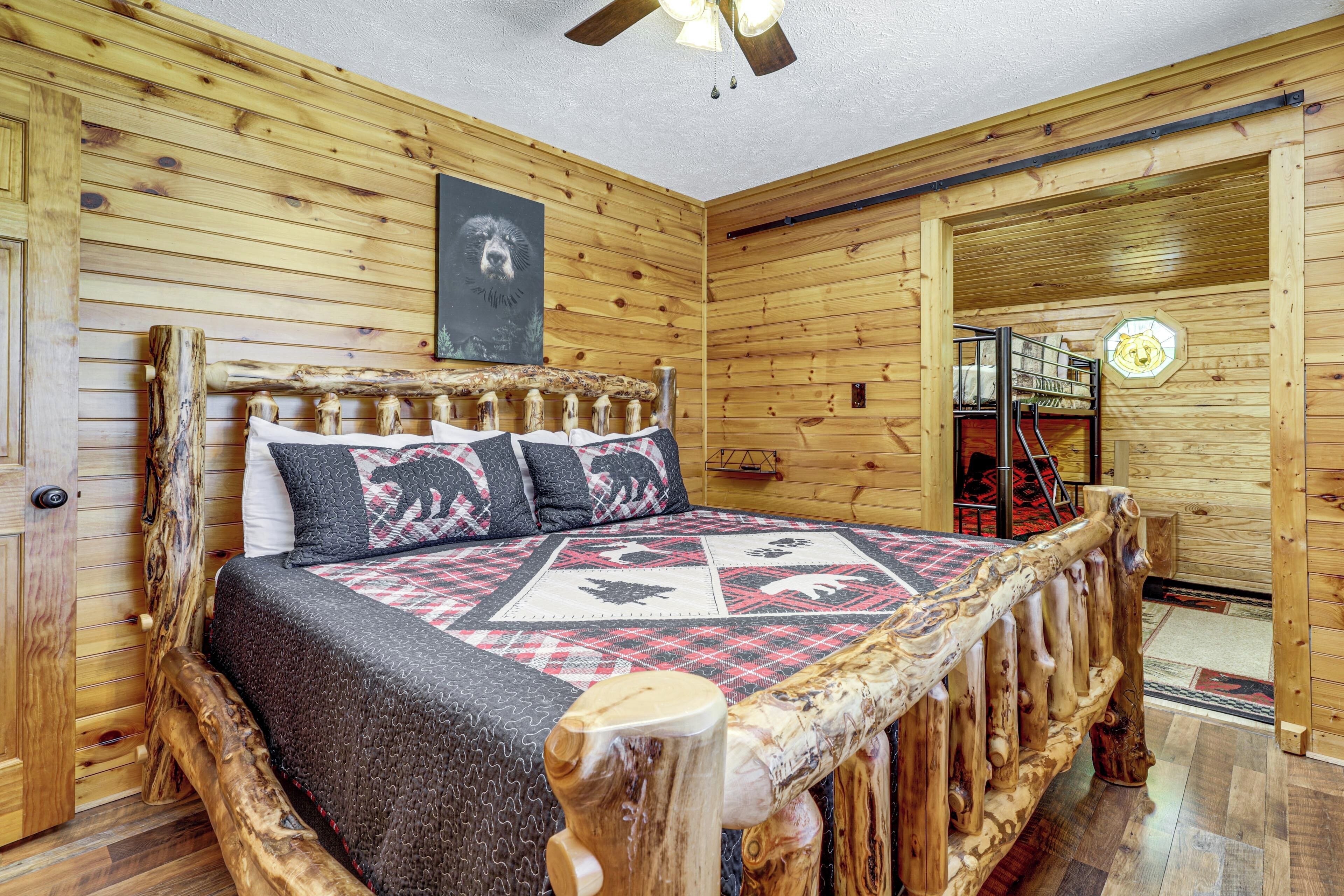 Une pièce de type cabane en bois, avec un lit, des murs en bois, un ventilateur de plafond et une porte en bois.