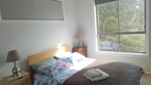A bedroom with a bed, a nightstand, a lamp, a window with a view of trees, and a wall-mounted shelf. - The Piddington Top (Mount Victoria)