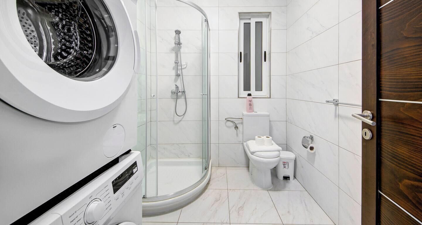 Ein kleines Badezimmer mit Waschmaschine, einer Duschkabine, Toilette und einer Holztür.