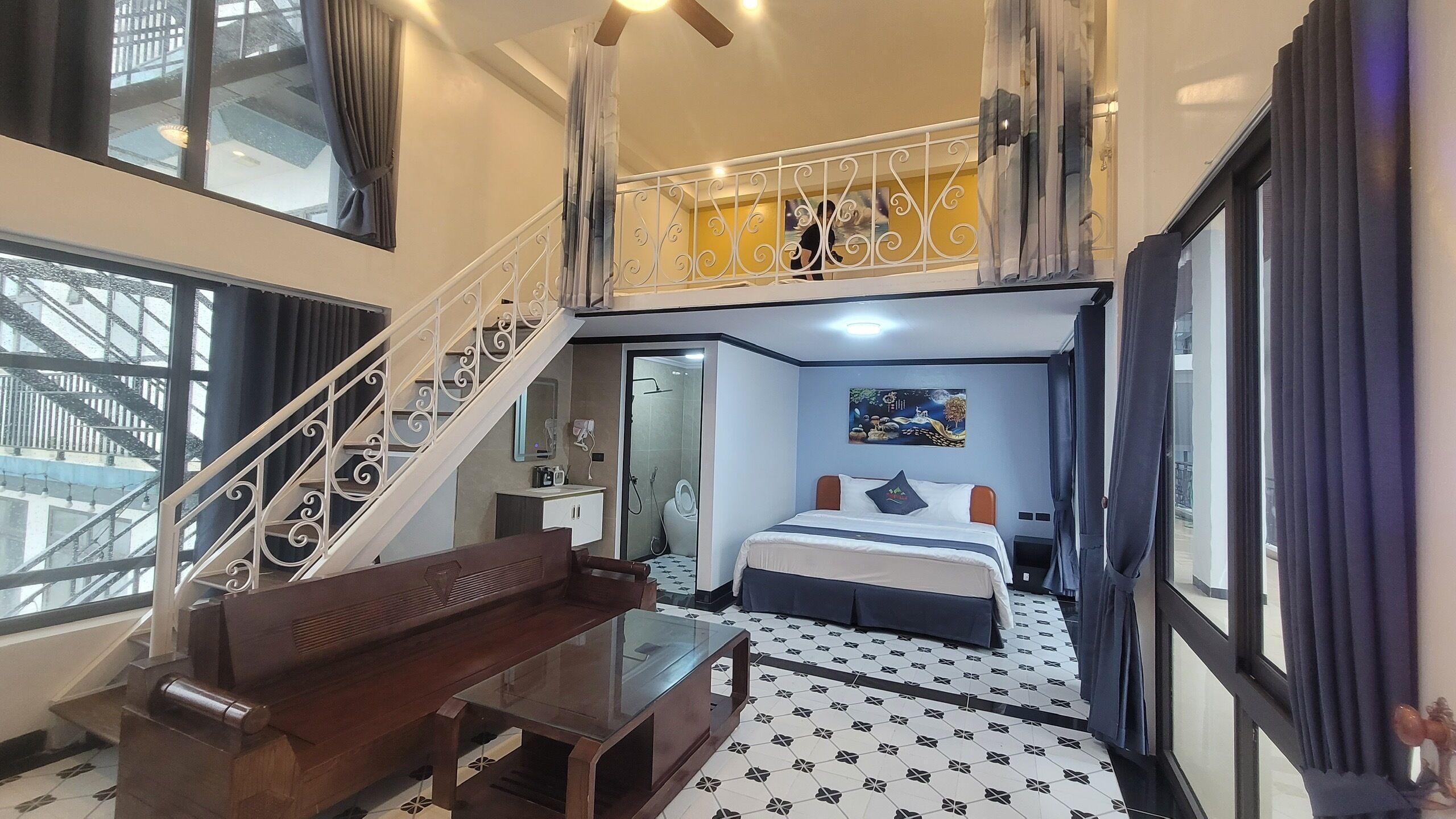 A hotel room with a bed, a desk, a chair, a balcony, and a staircase.
