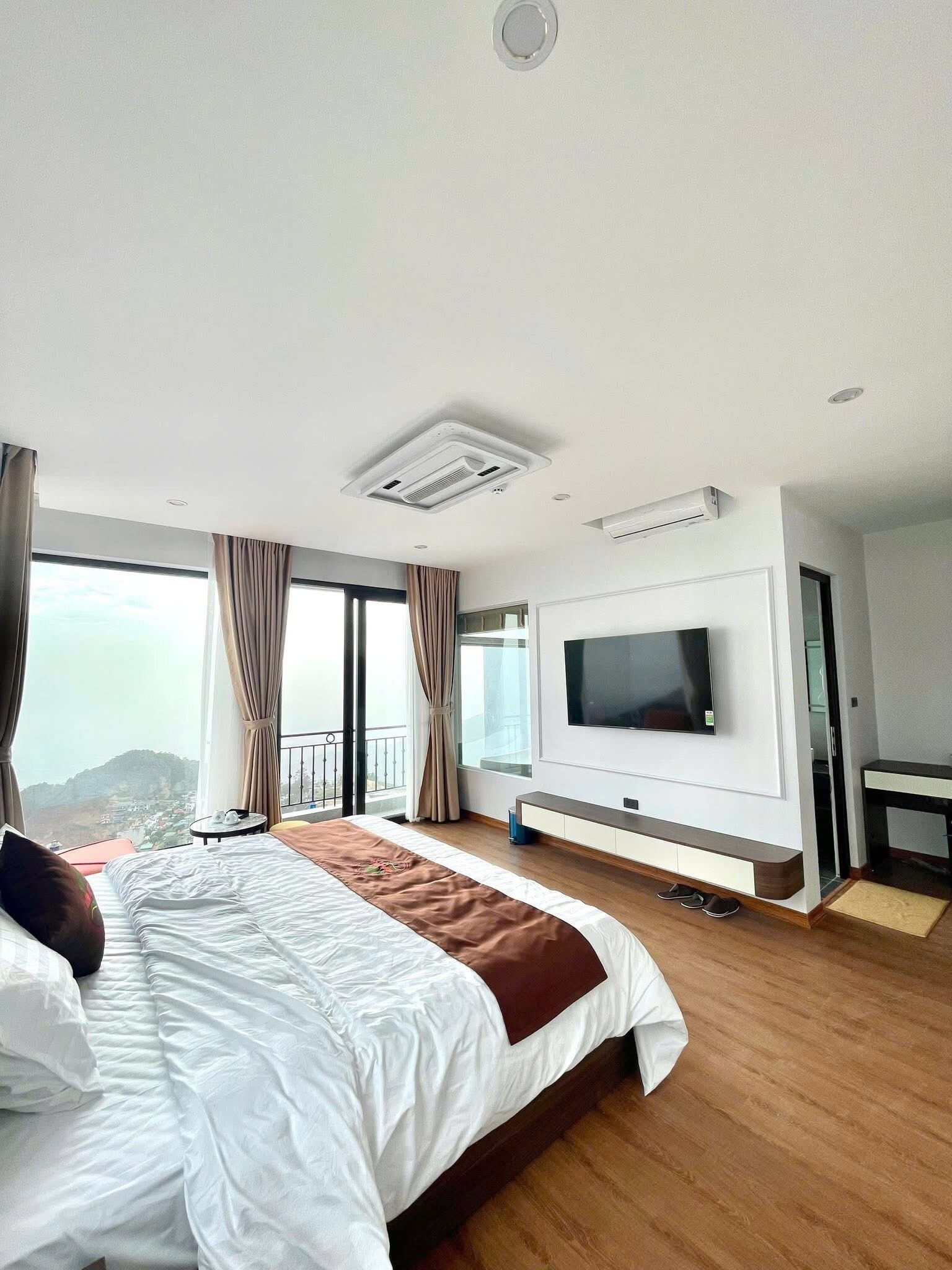 A modern hotel room with a large bed, a flat-screen TV, and a balcony with a view.