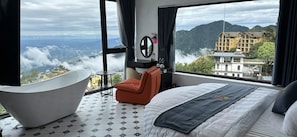 Een moderne hotelkamer met een groot bed, een ligbad en uitzicht op een bergachtig landschap.