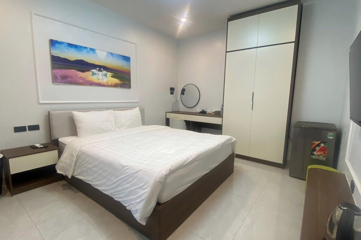 A hotel room with a bed, a nightstand, a dresser, a mirror, and a refrigerator.