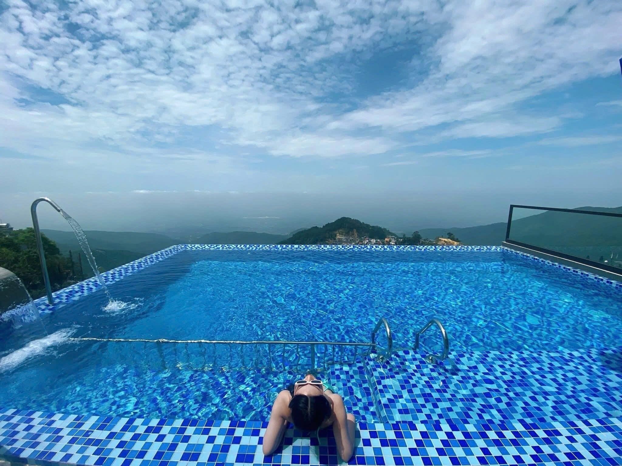 Une personne allongée sur le bord d’une piscine, avec vue sur un paysage montagneux.