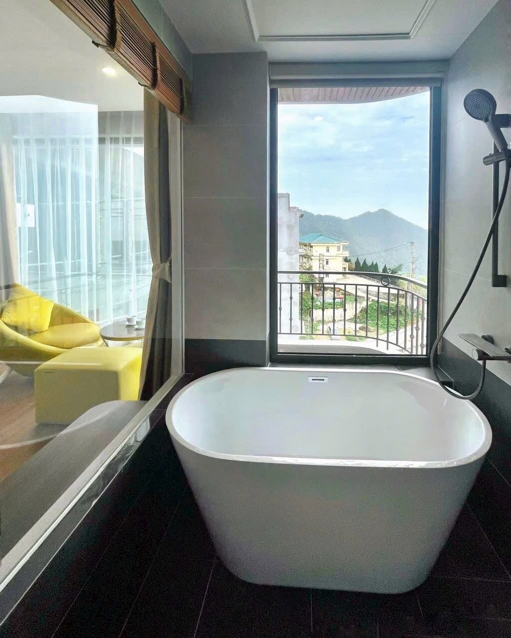 A modern bathroom with a freestanding bathtub, a shower area, and a view of a balcony with a cityscape.