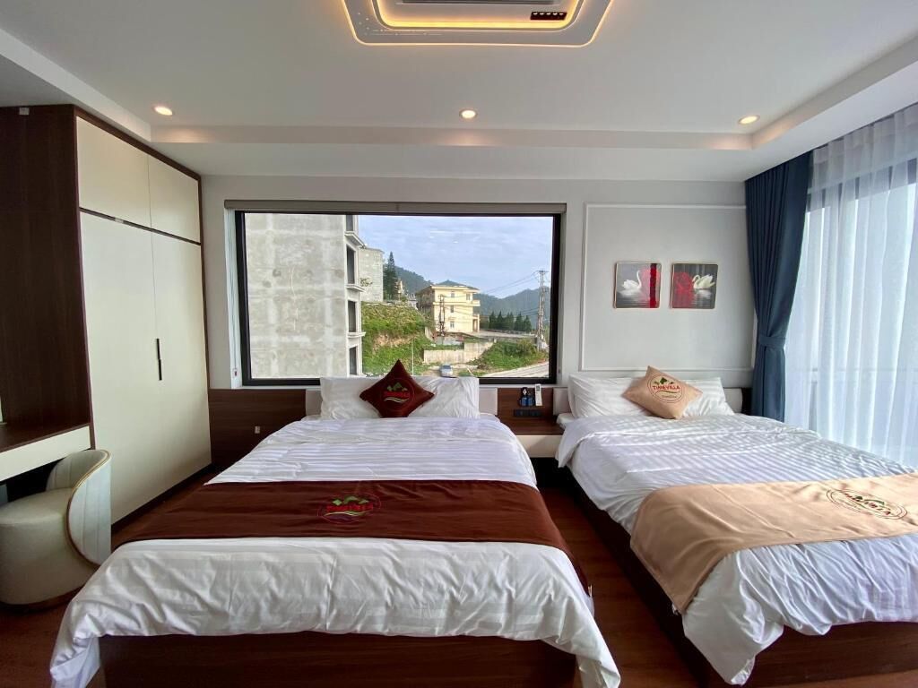A hotel room with two beds, a large window, and a view of buildings and mountains.