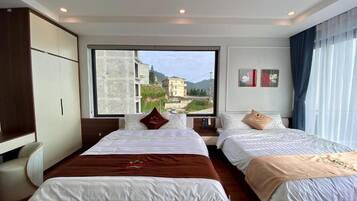 A hotel room with two beds, a large window, and a view of buildings and mountains.