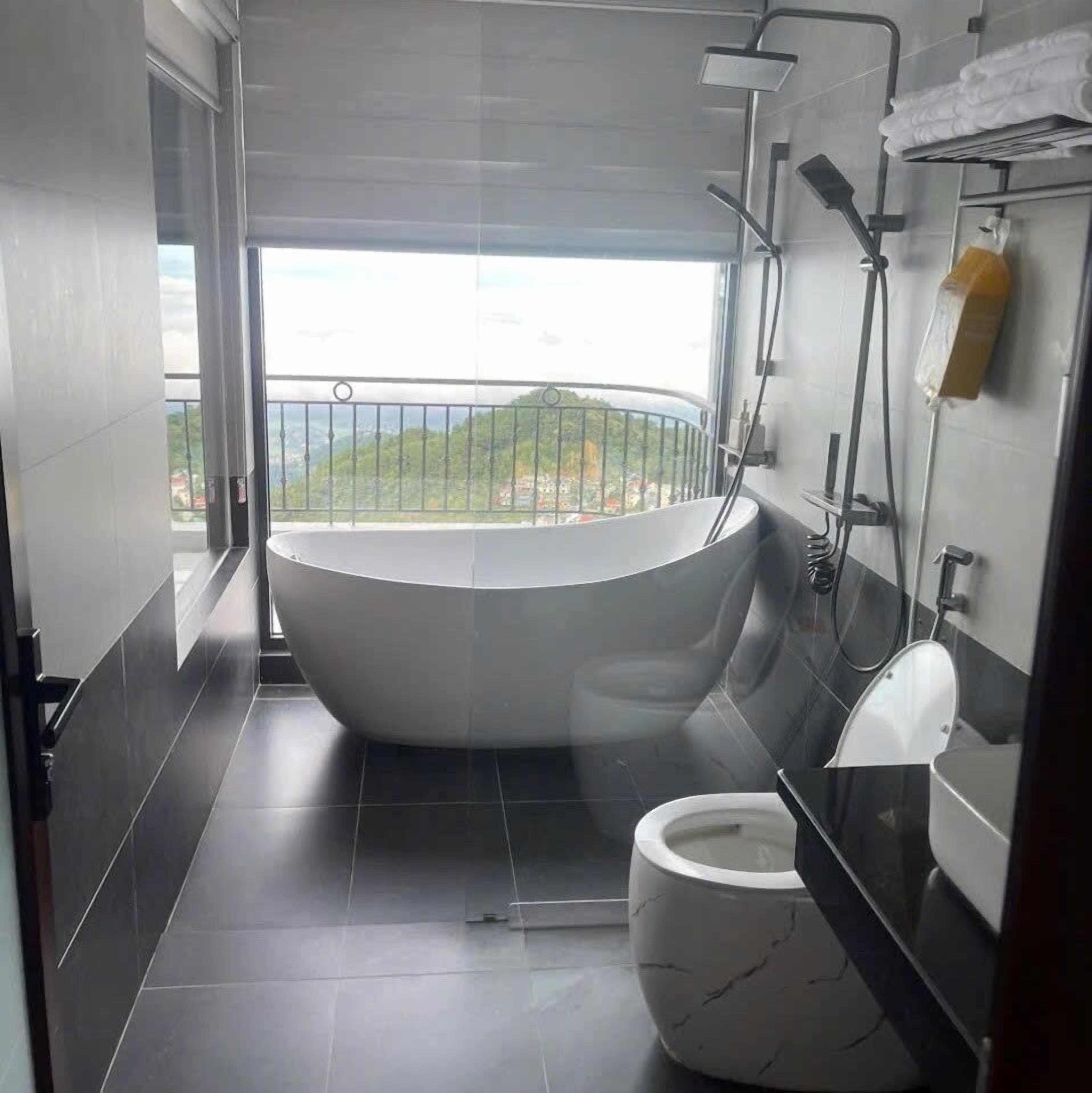 A modern bathroom with a bathtub, toilet, and a balcony with a view.