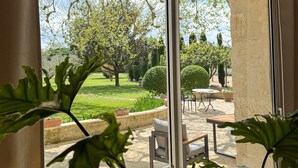 Ein Zimmer mit großen Fenstern und einer Gartenansicht, mit einem Tisch und Stühlen davor.