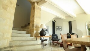 Eine Steintreppe führt zu einer erhöhten Ebene, ein schwarzer Tisch mit einer Lampe und ein schwarzer Stuhl befinden sich in einem Raum mit hoher Decke und Kamin.