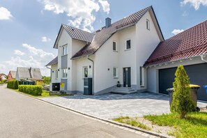 Et moderne hus i to etager med tegltag, en foranliggende garage og en lille forhave med en velplejet busk.