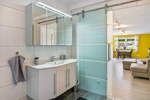 Ein modernes Badezimmer mit Duschkabine aus Glas, einem weißen Waschbecken und einem großen Spiegel.