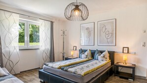 Quarto com cama grande, mesas de cabeceira com abajures, um candeeiro de chão e duas obras de arte nas paredes.