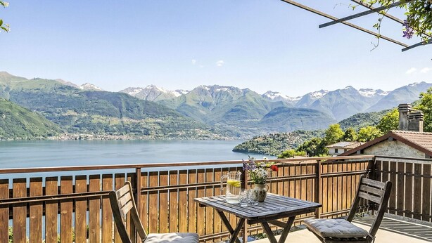 Terraço com mesa e duas cadeiras, com vista para um lago e montanhas.