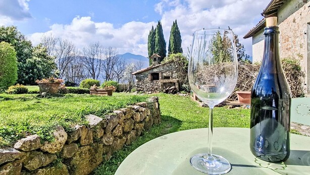 Un verre de vin sur une table, avec un mur en pierre et de la verdure en arrière-plan.
