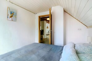 Ein Schlafzimmer mit Bett, einer Couch, einem Gemälde und einer Tür zu einem Küchenbereich.