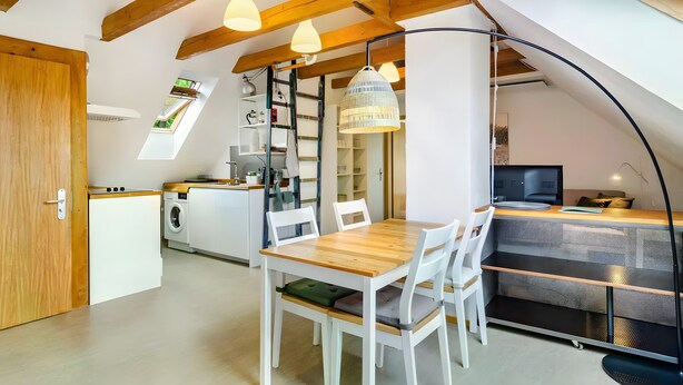 Une cuisine compacte avec un coin repas, des étagères intégrées et un espace nuit en mezzanine doté d’un puits de lumière.
