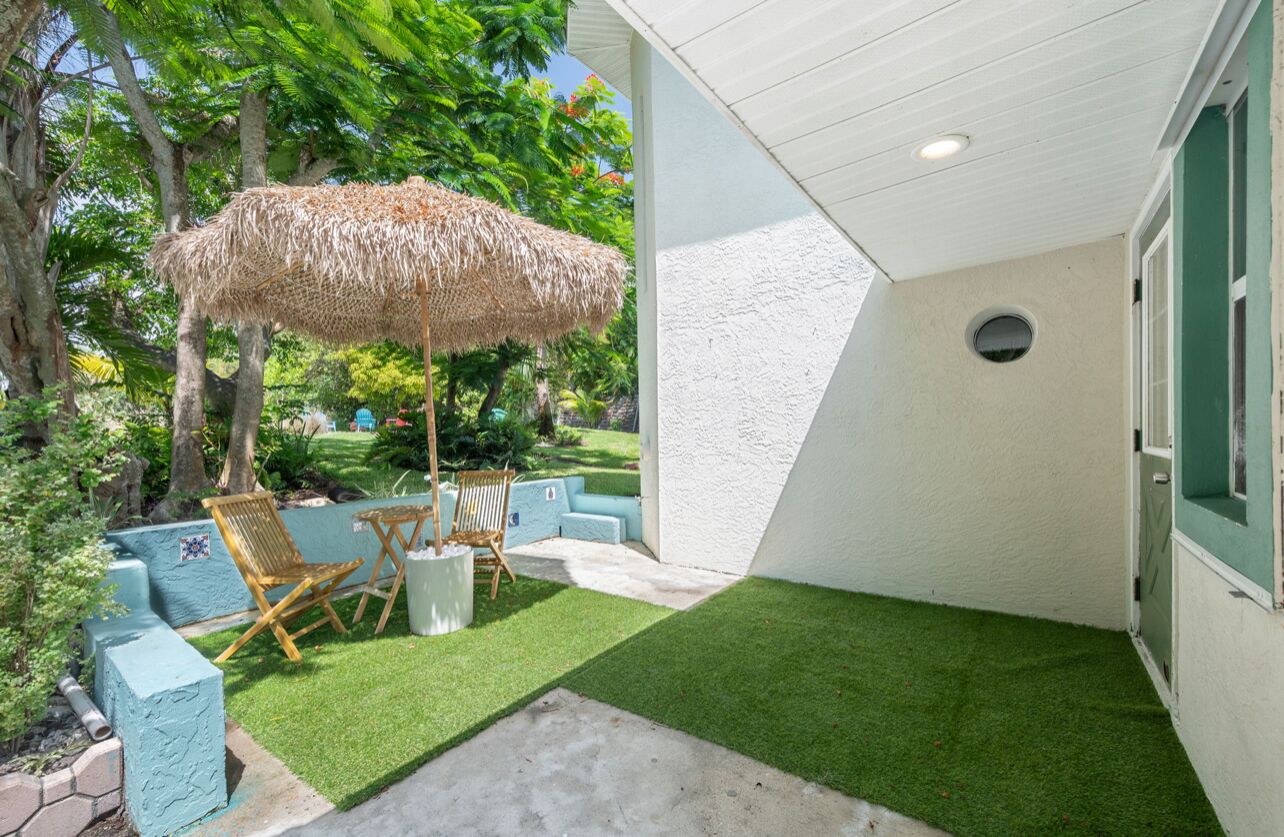 A patio with artificial grass, a thatched umbrella, and outdoor furniture.