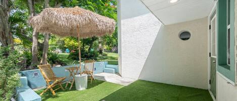 A patio with artificial grass, a thatched umbrella, and outdoor furniture.