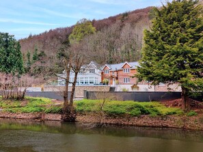 A lakeside property with a stone wall, a wooden house, and a large tree. - Stunning  villa for 6 guests with WIFI and pets allowed (Whitchurch)