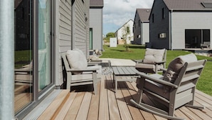 Een terras met buitenmeubilair, een glazen deur en uitzicht op omliggende huizen.