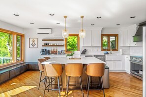 Una cocina moderna con una isla grande, taburetes de bar, armarios blancos y vistas al exterior.