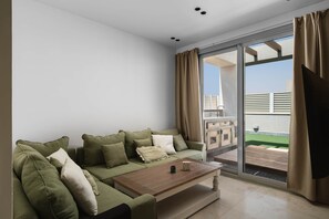 A modern living room with a green sofa set, a wooden coffee table, and a large sliding glass door leading to an outdoor balcony. - The White Pent - Palm Hills I Nesty Hospitality (New Cairo City)