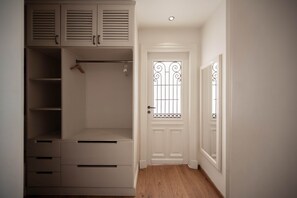 A walk-in closet with built-in shelving and drawers, a wooden hanger rod, and a door with decorative metal bars. - The White Pent - Palm Hills I Nesty Hospitality (New Cairo City)