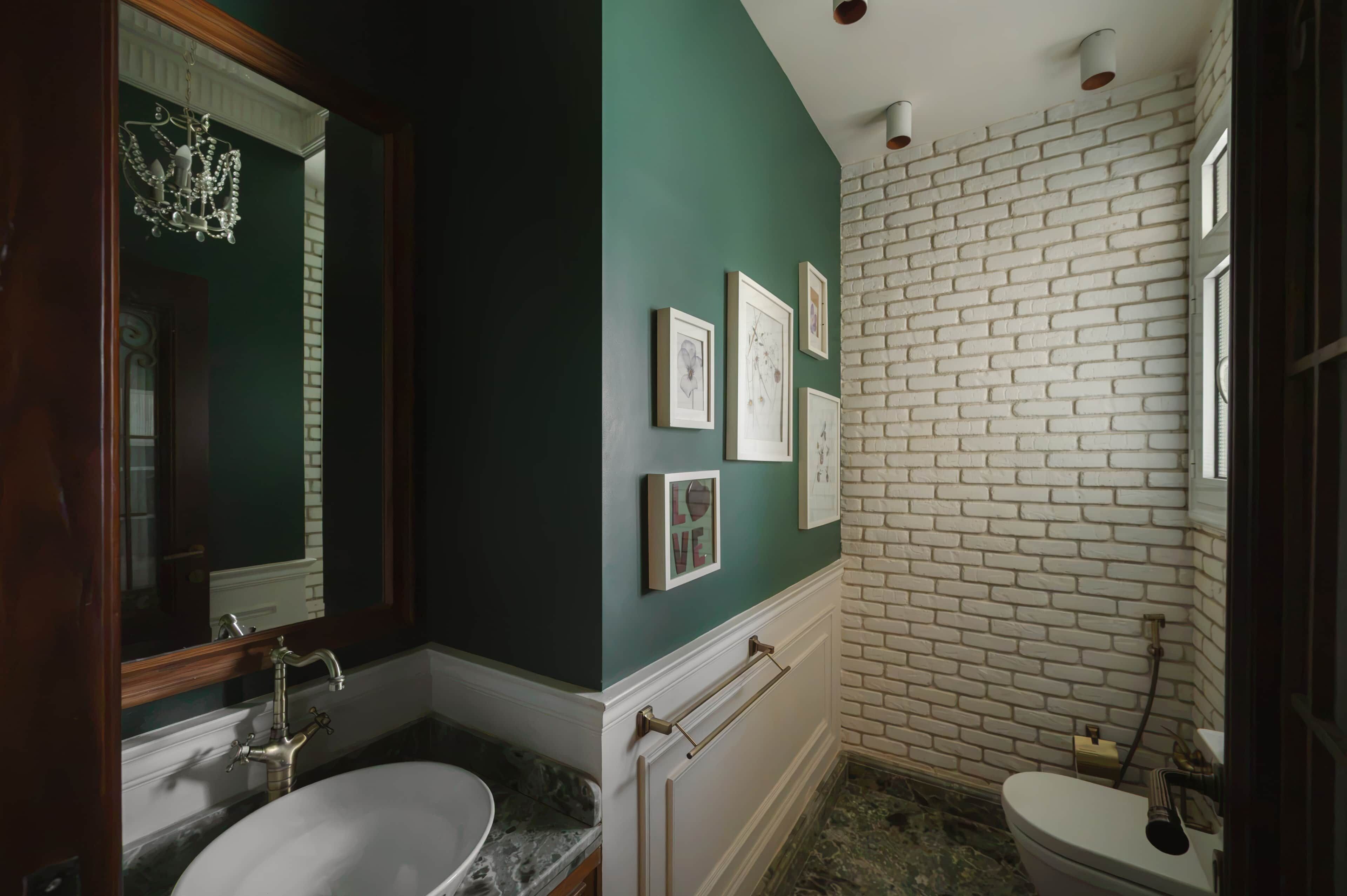 A bathroom with a white bathtub, a sink with a vintage faucet, and a toilet. There are framed pictures on the wall and a chandelier above the mirror.