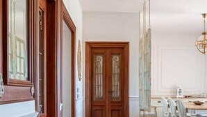 Ein Flur mit Holztüren, ein Essbereich mit weißen Stühlen und ein Sofa.