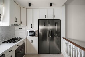 A kitchen with white cabinets, a stainless steel refrigerator, a microwave, and a gas stove. - The White Pent - Palm Hills I Nesty Hospitality (New Cairo City)