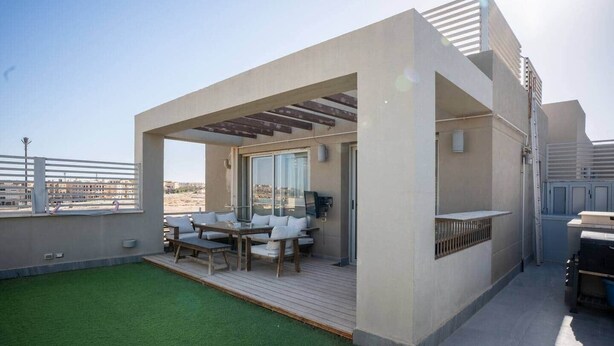 Eine Dachterrasse mit Holzdeck, Sitzmöbeln im Freien und Blick auf die Stadt.