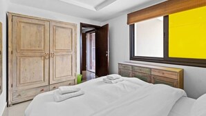 A bedroom with a large wardrobe, a bed with white linens, and a window with a yellow view.