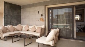 A modern outdoor seating area with a sofa and chairs, a glass table, and a sliding glass door leading to an indoor space.