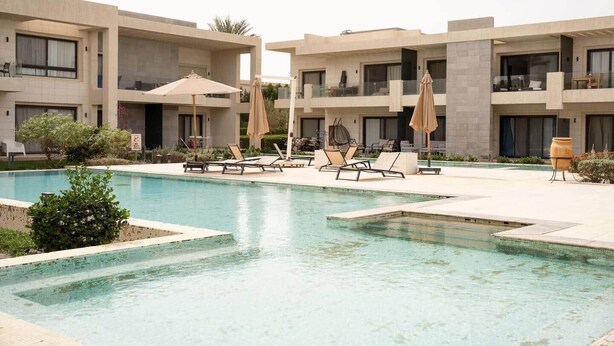 A modern hotel with a swimming pool, sun loungers, and umbrellas.