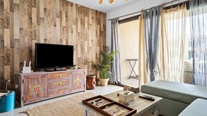 A living room with a wooden wall, a flat-screen TV, a sofa, a coffee table with a board game, and a potted plant.