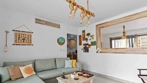 A living room with a sofa, a coffee table, a hanging light fixture, a wall-mounted mirror, and a wall decoration.