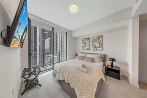 A modern bedroom with a large bed, a flat-screen TV mounted on the wall, a balcony with a view of buildings, and abstract wall art. - Sleek 1BR | Free Parking | FIFA Fan Fest Walk (Miami)