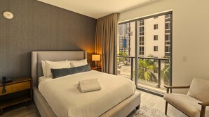 Een hotelkamer met een groot bed, een nachtkastje, een stoel, een raam met uitzicht op gebouwen en een balkon.