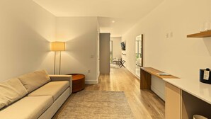 Een moderne woonkamer met een bank, een lamp, een houten salontafel en een keuken met een aanrecht en kastjes.