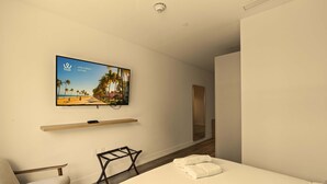 Een hotelkamer met een bed, een stoel, een aan de muur bevestigde televisie en een houten plank.
