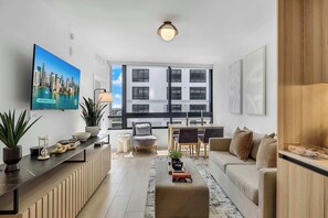 Una sala de estar moderna con televisor, sofá, mesa de comedor, sillas y un ventanal con vistas a la ciudad.