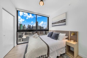 Un dormitorio con un ventanal grande, una cama, una mesita de noche y una lámpara de pared.