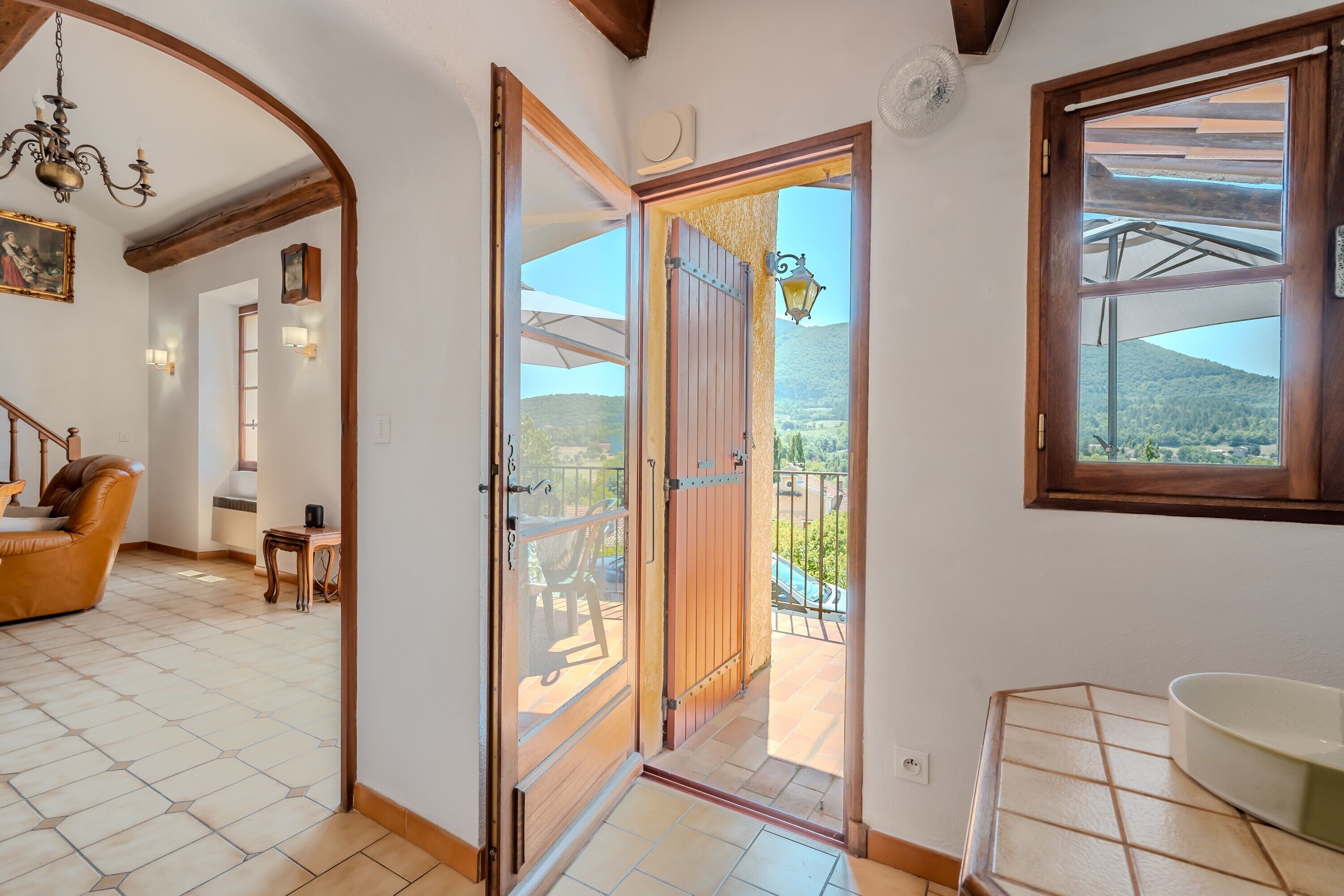 Ein Zimmer mit einer Holztür, die auf einen Balkon mit Blick ins Grüne führt.