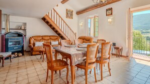 Un espace repas comprenant une table et des chaises en bois, une cheminée et un escalier menant à un niveau supérieur.