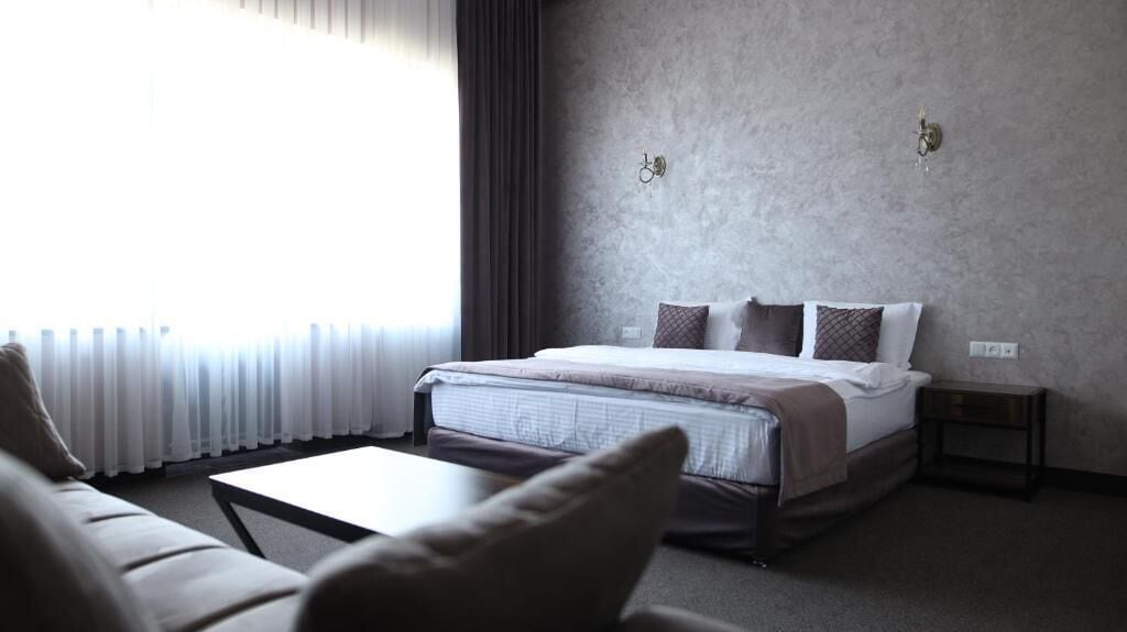 A hotel room with a bed, a bedside table, a small table, and a sofa.