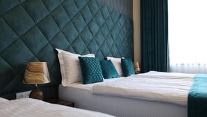 A hotel room with a quilted headboard, a bed with white bedding, and a nightstand with a lamp. - BMG Hotel  (Goris)